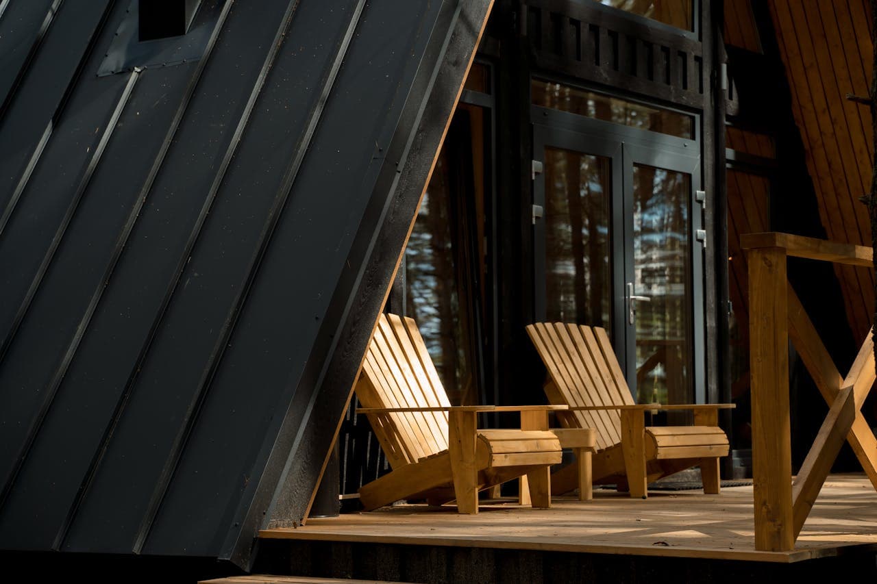 Two Adirondack chairs sit on the porch of a black house